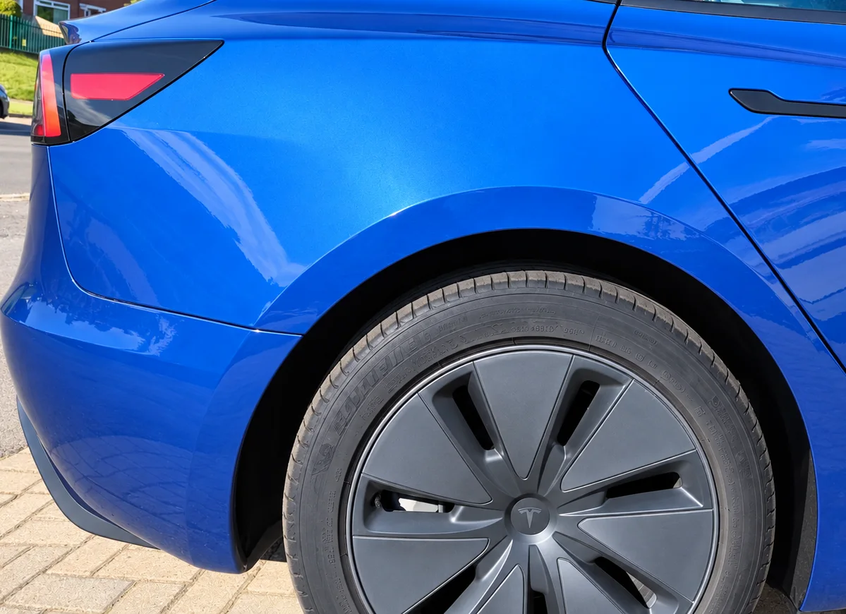 The same Tesla Model 3 rear quarter panel after repair, resprayed in metallic blue with the arch line restored