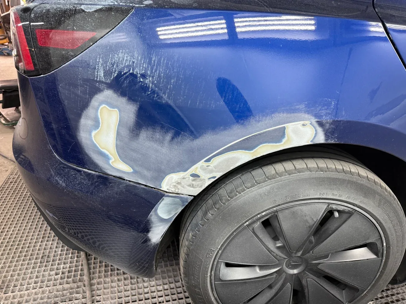 Rear quarter panel of a blue Tesla Model 3 in the workshop, body filler applied and the paint sanded back around the wheel arch