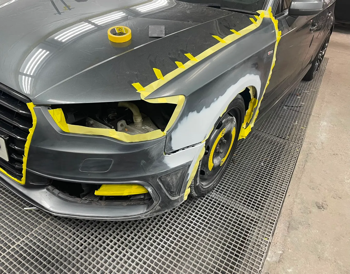 Grey Audi A3 mid-repair with the headlight removed, the front wing in primer and the bumper masked with tape
