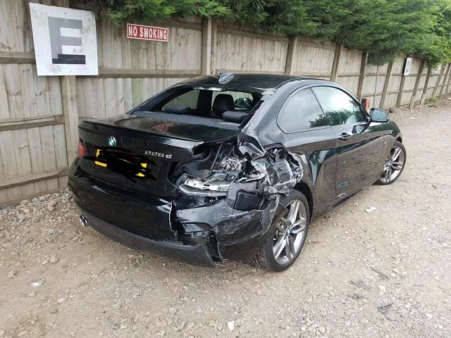 Black BMW 225d coupe with heavy rear-end collision damage, the rear quarter panel crushed and the bumper hanging off